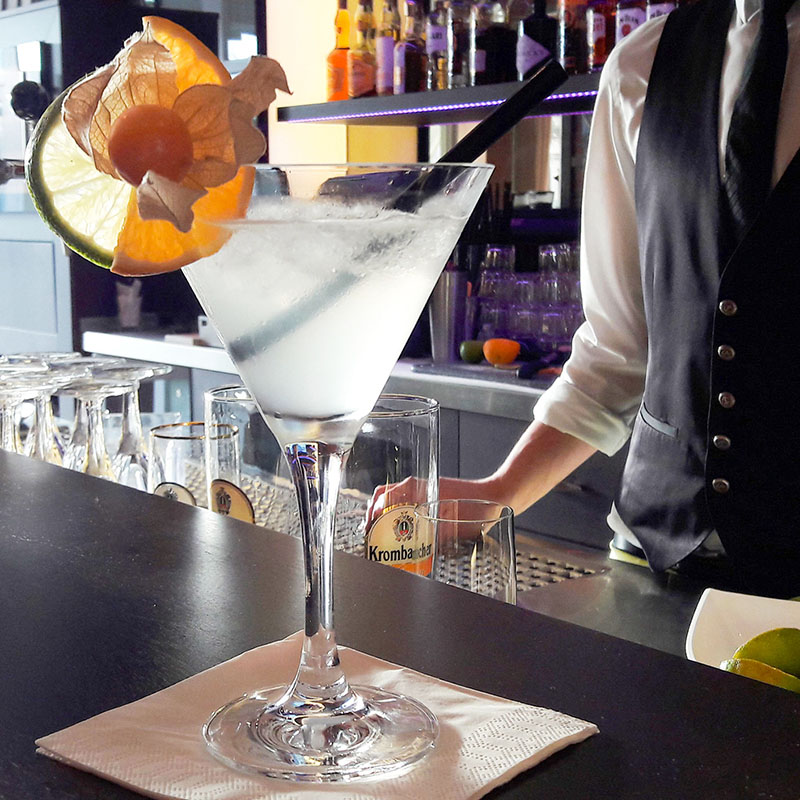 Ein Glas Martini auf dem Bartresen mit einem Kellner im Hintergrund
